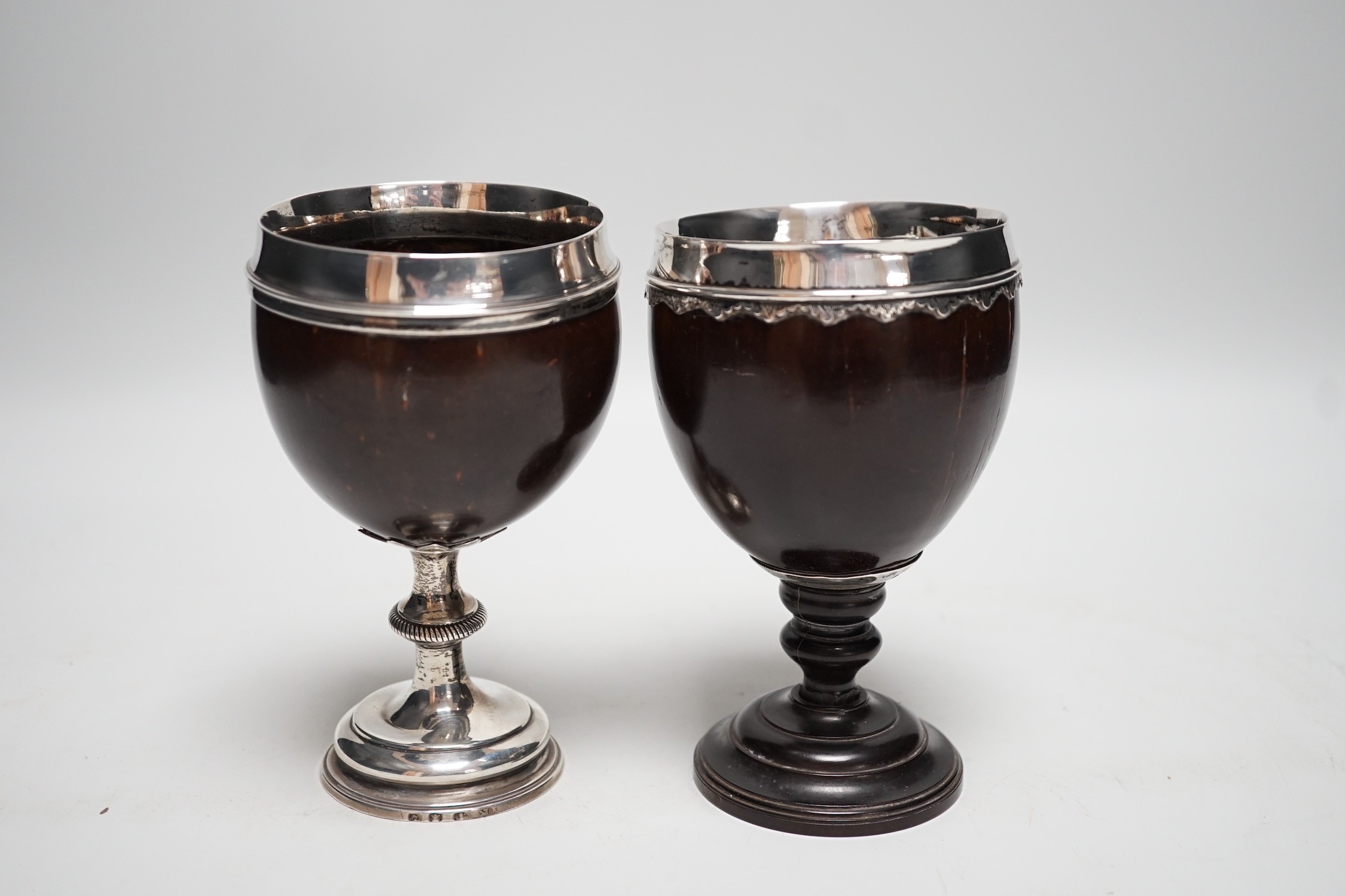 Two late 18th century white metal mounted pedestal coconut cups, one hallmarked silver for John Robbins?, London, 1764, 14.4cm, the other with white metal mounted top rim, on turned wooden base.